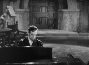 Movie still from “The Most Dangerous Game” (1932), directed by Irving Pichel – A black and white photo of a man sitting at a piano; Medium shot, High angle