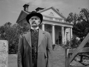 Movie still from “The Ox-Bow Incident” (1942), directed by William A. Wellman – A man in a suit and hat standing in front of a house; Medium shot, Low angle