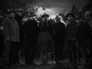 Movie still from “The Ox-Bow Incident” (1942), directed by William A. Wellman – A black and white photo of a group of men standing in a field; Wide shot, Low angle