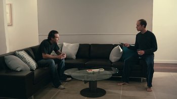 Movie still from “The Perfect Host” (2010), directed by Nicholas Tomnay – Two people sitting on a couch in a living room; Wide shot, High angle