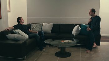 Movie still from “The Perfect Host” (2010), directed by Nicholas Tomnay – A man sitting on a couch in a living room; Wide shot, High angle