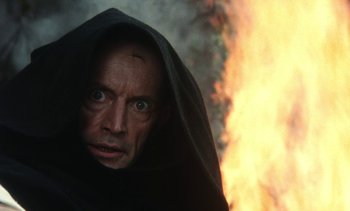 Movie still from “The Pit and the Pendulum” (1991), directed by Stuart Gordon – A man in a black robe with a fire behind him; Close Up shot, Low angle