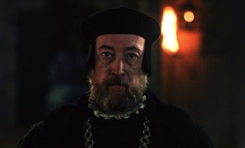 Movie still from “The Pit and the Pendulum” (1991), directed by Stuart Gordon – A man with a long beard wearing a black hat; Close Up shot, Over the shoulder angle