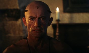 Movie still from “The Pit and the Pendulum” (1991), directed by Stuart Gordon – A man with a bald head is looking at the camera; Close Up shot, Low angle