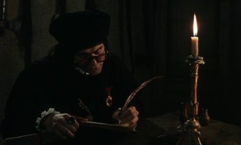 Movie still from “The Pit and the Pendulum” (1991), directed by Stuart Gordon – A man writing on a piece of paper next to a lit candle; Medium shot, Over the shoulder angle