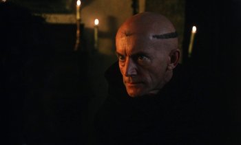 Movie still from “The Pit and the Pendulum” (1991), directed by Stuart Gordon – A man with a shaved head is looking at the camera; Close Up shot, Low angle