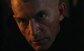 Movie still from “The Pit and the Pendulum” (1991), directed by Stuart Gordon – A man with a shaved head and a black shirt; Close Up shot, Low angle