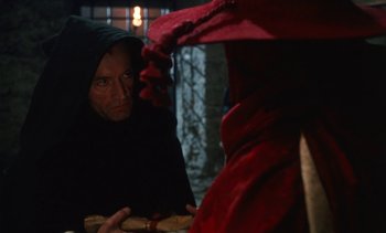 Movie still from “The Pit and the Pendulum” (1991), directed by Stuart Gordon – A man in a hooded cloak looking at another man in a red robe; Close Up shot, Over the shoulder angle