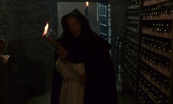Movie still from “The Pit and the Pendulum” (1991), directed by Stuart Gordon – A man in a hooded cloak holding a burning stick; Medium shot, Low angle