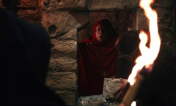 Movie still from “The Pit and the Pendulum” (1991), directed by Stuart Gordon – A woman wearing a red robe and a red head covering is looking out a window; Medium shot, Over the shoulder angle