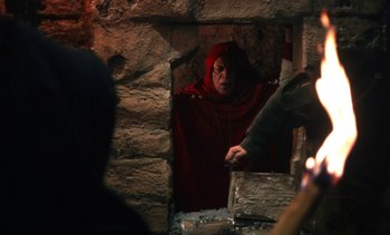 Movie still from “The Pit and the Pendulum” (1991), directed by Stuart Gordon – An older woman in a red cape looking into a window; Medium shot, Over the shoulder angle