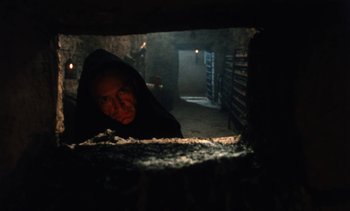 Movie still from “The Pit and the Pendulum” (1991), directed by Stuart Gordon – A man in a black hooded jacket looking out of an oven in a dark room; Close Up shot, Low angle