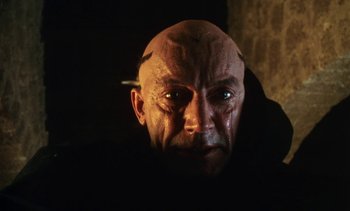 Movie still from “The Pit and the Pendulum” (1991), directed by Stuart Gordon – A man with a bald head and a cigarette in his mouth; Close Up shot, High angle