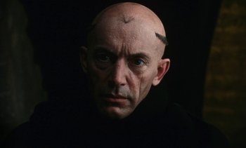 Movie still from “The Pit and the Pendulum” (1991), directed by Stuart Gordon – A man with a shaved head and a shaved head is looking at the camera; Close Up shot, High angle