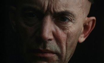 Movie still from “The Pit and the Pendulum” (1991), directed by Stuart Gordon – An old man with a shaved head and a goatee looking at the camera; Extreme Close Up shot, Low angle