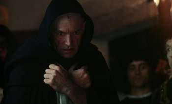 Movie still from “The Pit and the Pendulum” (1991), directed by Stuart Gordon – A man in a black hooded cloak with a knife in his hand; Close Up shot, High angle