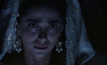 Movie still from “The Pit and the Pendulum” (1991), directed by Stuart Gordon – A young woman with dark hair wearing a dress and earrings; Close Up shot, High angle