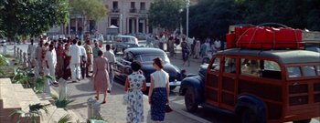 Movie still from “The Rains of Ranchipur” (1955), directed by Jean Negulesco – A group of women walking down a street past parked cars; Extreme Wide shot, High angle