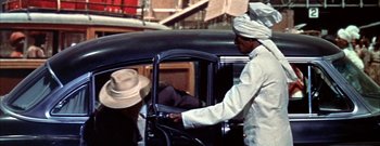 Movie still from “The Rains of Ranchipur” (1955), directed by Jean Negulesco – A man in a white hat is driving a black car; Medium shot, High angle