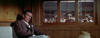 Movie still from “The Rains of Ranchipur” (1955), directed by Jean Negulesco – A man sitting in front of a window with people in the background; Medium shot, Over the shoulder angle