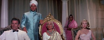Movie still from “The Rains of Ranchipur” (1955), directed by Jean Negulesco – An older woman sitting in a chair in front of two other people; Medium shot, Low angle