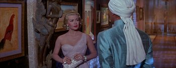 Movie still from “The Rains of Ranchipur” (1955), directed by Jean Negulesco – A woman in a white dress talking to a man in a white turban; Medium shot, Over the shoulder angle