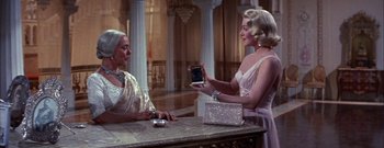 Movie still from “The Rains of Ranchipur” (1955), directed by Jean Negulesco – Two women are sitting at a table and one of them is holding up a cell phone; Medium shot, Over the shoulder angle