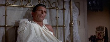 Movie still from “The Rains of Ranchipur” (1955), directed by Jean Negulesco – A man sitting on a bed wearing a toga; Close Up shot, High angle