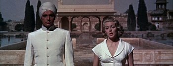Movie still from “The Rains of Ranchipur” (1955), directed by Jean Negulesco – A woman and a man standing next to each other in front of a building; Medium shot, Low angle