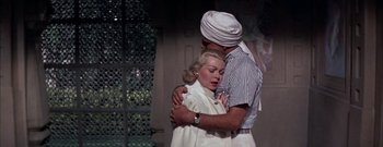 Movie still from “The Rains of Ranchipur” (1955), directed by Jean Negulesco – A man and a woman embracing each other in front of a building; Medium shot, Low angle