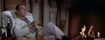 Movie still from “The Rains of Ranchipur” (1955), directed by Jean Negulesco – A man sitting on a chair with a glass of wine; Medium shot, High angle