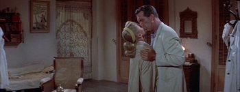 Movie still from “The Rains of Ranchipur” (1955), directed by Jean Negulesco – A man and a woman standing next to each other in a room; Medium shot, High angle