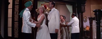 Movie still from “The Rains of Ranchipur” (1955), directed by Jean Negulesco – A man and a woman in a white suit and a man and a woman in a white suit and a man in a white suit; Medium shot, Over the shoulder angle