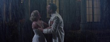 Movie still from “The Rains of Ranchipur” (1955), directed by Jean Negulesco – A man and a woman dancing in the rain in front of a window; Wide shot, Low angle