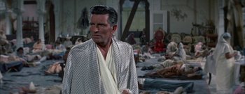 Movie still from “The Rains of Ranchipur” (1955), directed by Jean Negulesco – An older man wearing a robe in front of a room filled with people; Medium shot, High angle