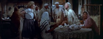 Movie still from “The Rains of Ranchipur” (1955), directed by Jean Negulesco – A group of people standing around a table with food on top of it; Medium shot, High angle