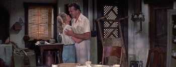 Movie still from “The Rains of Ranchipur” (1955), directed by Jean Negulesco – A man and a woman embracing in front of a chair; Medium shot, Low angle