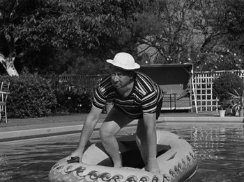 Movie still from “The Reluctant Dragon” (1941), directed by Jack Cutting – A black and white photo of a man on a raft in a pool; Medium shot, High angle