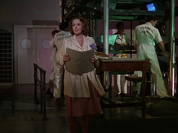 Movie still from “The Reluctant Dragon” (1941), directed by Jack Cutting – A woman holding a sheet of paper while standing next to a table; Medium shot, Low angle