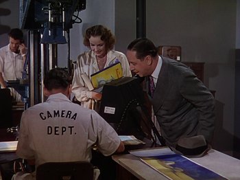 Movie still from “The Reluctant Dragon” (1941), directed by Jack Cutting – Two men and a woman are looking at some papers; Medium shot, Over the shoulder angle