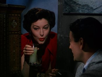 Movie still from “The Snows of Kilimanjaro” (1952), directed by Henry King – A woman in a red jacket drinking a drink; Close Up shot, Over the shoulder angle
