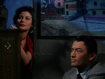 Movie still from “The Snows of Kilimanjaro” (1952), directed by Henry King – A man and a woman are sitting next to each other in front of a painting; Medium shot, Low angle