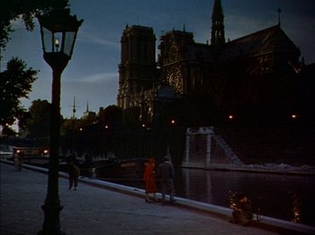Movie still from “The Snows of Kilimanjaro” (1952), directed by Henry King – Two people standing on the side of a river near a building; Extreme Wide shot, High angle