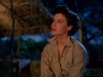 Movie still from “The Snows of Kilimanjaro” (1952), directed by Henry King – A woman sitting in front of a palm tree at night; Close Up shot, Low angle
