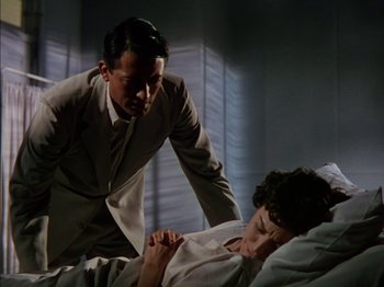 Movie still from “The Snows of Kilimanjaro” (1952), directed by Henry King – A man in a suit and tie standing next to a woman in a bed; Medium shot, Low angle