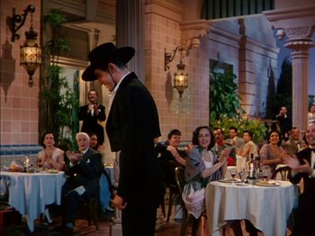 Movie still from “The Snows of Kilimanjaro” (1952), directed by Henry King – A group of people sitting at a table with food; Wide shot, Over the shoulder angle