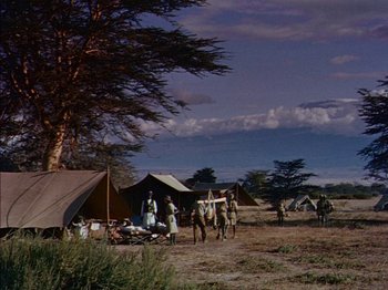 Movie still from “The Snows of Kilimanjaro” (1952), directed by Henry King – A group of people standing next to tents on a dirt field; Extreme Wide shot, Low angle
