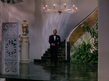 Movie still from “The Snows of Kilimanjaro” (1952), directed by Henry King – A man in a suit standing in front of a staircase; Wide shot, Low angle
