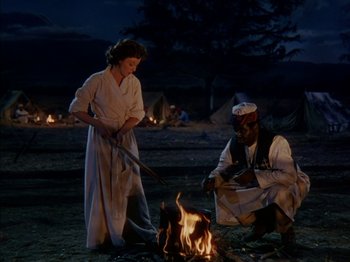 Movie still from “The Snows of Kilimanjaro” (1952), directed by Henry King – A man and a woman standing next to a fire; Wide shot, High angle