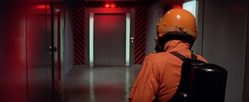 Movie still from “The Swarm” (1978), directed by Irwin Allen – A person wearing a helmet in an elevator room; Medium shot, Low angle
